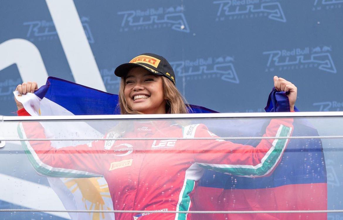 Filipina woman won a race and is standing on a platform holding up a Filipino flag with happiness